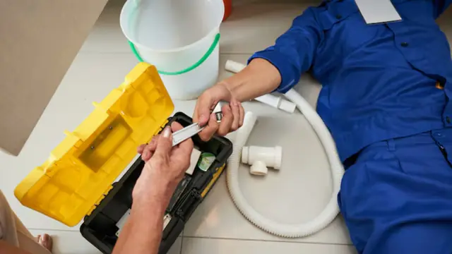 Technician working on white drain tubing with a bucket and toolbox